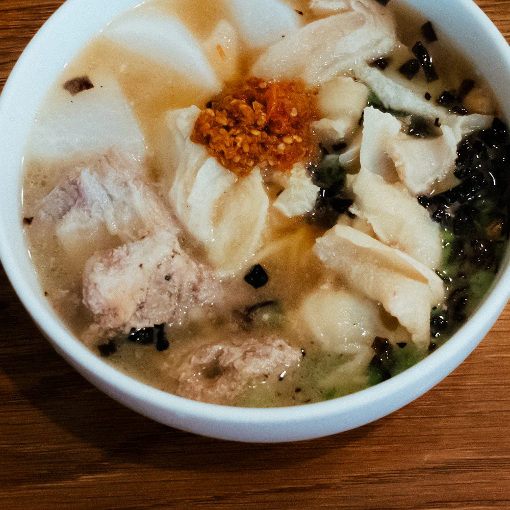 흰 대접에 담긴 만둣국. 떡과 만두, 다진 양념이 함께 올라가 있다