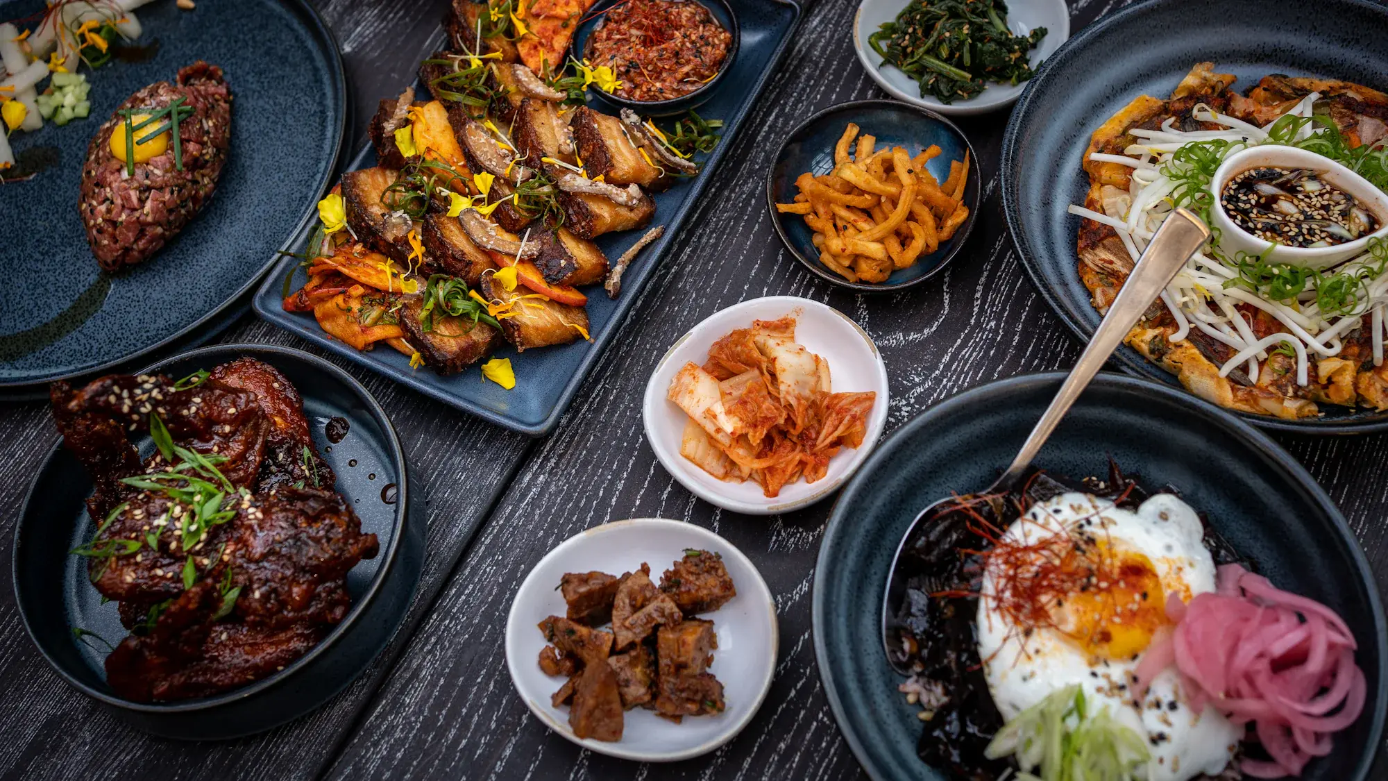 검은 우물마루 위에 놓인 여름 한상. 육회와 수육, 나물과 부침이 반상기에 나뉘어 담겨 있다