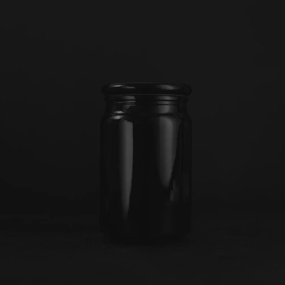 검은 배경 위에 놓인 무광 흑색 유리 크림 용기